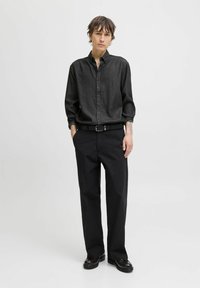 Cămașă neagră cu butoni, cu mâneci lungi, confecționată dintr-un material texturat. Pur tată cu pantaloni negri, largi și pantofi negri. Design minimalist.