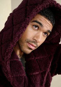 Ung mand med kort krøllet hår iført en blød, mørk lilla hættetrøje, der kigger opad med et eftertænksomt udtryk.