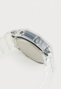 Montre numérique en plastique transparent avec matériel argenté, cadran rectangulaire, mécanisme exposé et bracelet transparent.
