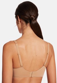 Nude-farvet bh med justerbare stropper, glat stof og en hægte-og-øje lukning på ryggen. Har en rund form og et minimalistisk design.