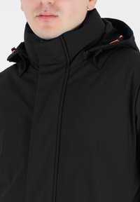 Giacca softshell nera con colletto alto, dettagli arancioni a contrasto e un design elegante. Dispone di una zip e di un cappuccio regolabile.