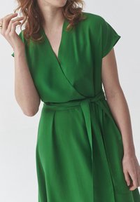 Rochie verde împăturată din țesătură netedă, cu mâneci scurte și o curea asortată. Prezintă un decolteu în V și un design fluid pentru un fit confortabil.