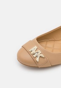 Chaussure plate beige avec doublure intérieure matelassée et logo MK doré sur la bride avant, vue depuis l'angle supérieur.
