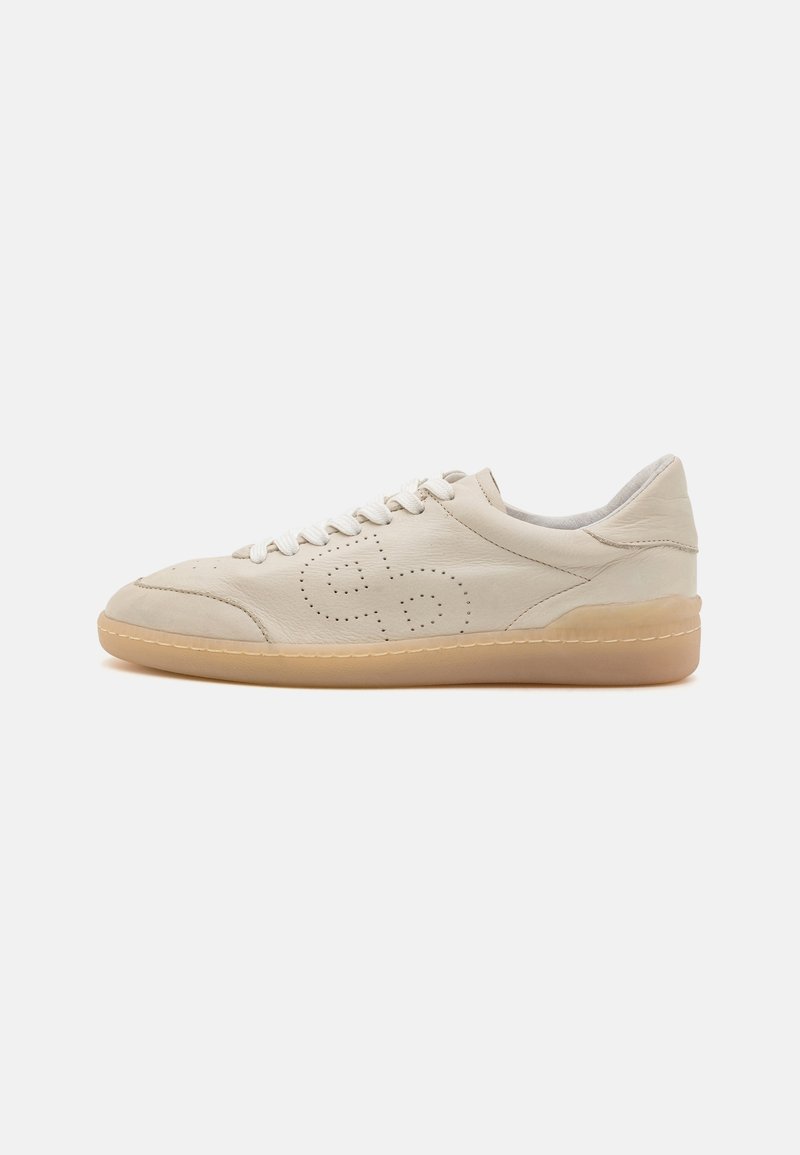 Baskets basses en cuir beige avec design latéral perforé, lacets blancs et semelle en caoutchouc marron clair, vues de profil sur fond blanc.
