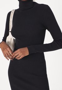 Robe noire côtelée à col roulé avec manches longues. Le tissu semble doux, la silhouette ajustée met en valeur le corps et possède une texture lisse.