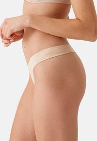 Beige string ondergoed met een zachte, gladde textuur en een smalle tailleband, met een minimalistisch ontwerp en zonder zichtbare patronen of hardware.