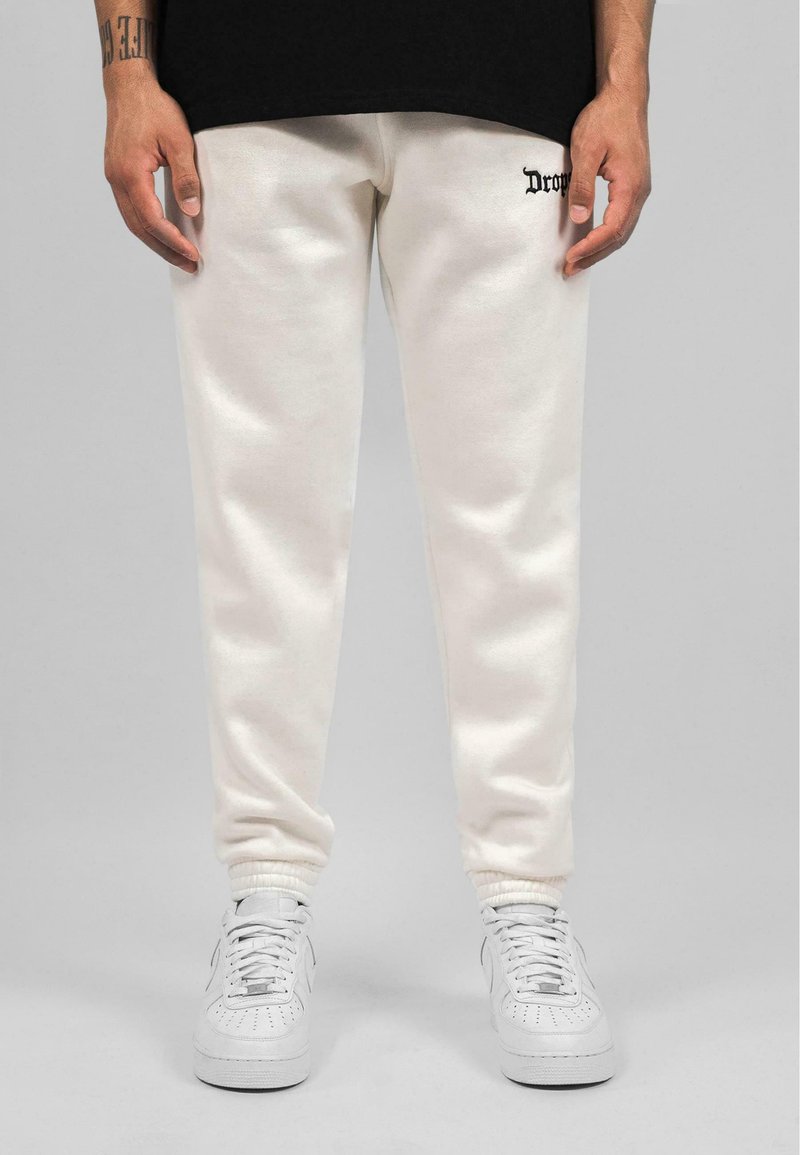 Hvide bomulds sweatpants med ribbet mansjetter, med et lille sort logo på venstre lår. Kombineret med hvide sneakers.