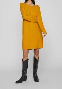 Senapsgul stickad klänning med långa ärmar, rund halsringning, ribbat avslut, kombinerad med knähöga svarta läderstövlar med sidsynk.