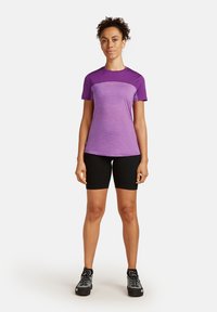 T-shirt de sport violet avec un design dégradé, manches courtes, et shorts de vélo noirs. La tenue comprend des chaussures de randonnée noires avec une surface texturée.