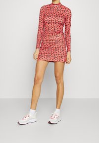 Red leopard print dress with long sleeves and mock neck, paired with white athletic shoes featuring pink accents and white socks.