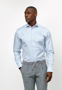 Lichtblauw overhemd met lange mouwen en knoopsluiting, gemaakt van een soepele stof, gecombineerd met grijze op maat gemaakte broek met een trekkoord in de taille.