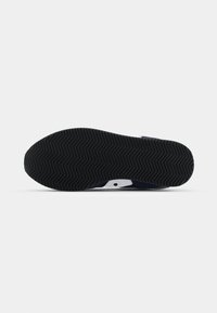 Black rubber shoe sole with herringbone pattern, featuring a white accent and navy blue side panel. Flat design for stability.