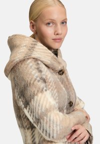 Beige und brauner karierter Wollmantel mit einer großen Kapuze, zwei Knöpfen und einer weichen Textur. Verfügt über einen lockeren Schnitt und sichtbare Nahtdetails.