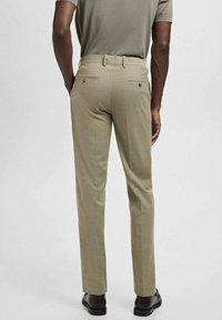 Beiga byxor i strukturerad tyg med rak passform, två bakfickor med knäppning och som bärs med svarta skor.