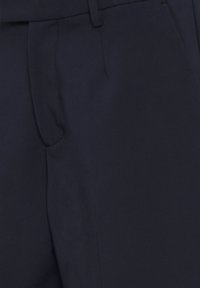 Gros plan sur un pantalon bleu marine montrant la poche avant, la ceinture avec passants pour ceinture et la texture du tissu.