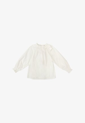 Blusa blanca de manga larga con un escote volante y detalle de moño en el hombro. Tejido suave con puños elásticos y corte holgado.