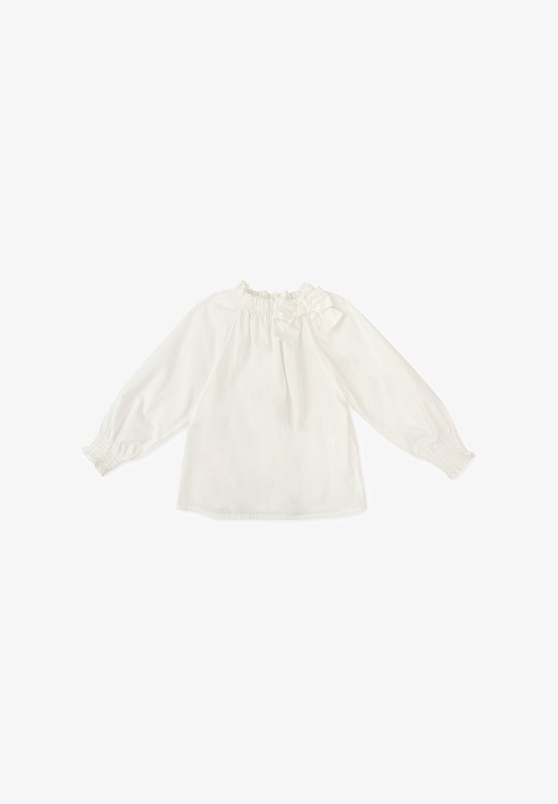 Blusa blanca de manga larga con un escote volante y detalle de moño en el hombro. Tejido suave con puños elásticos y corte holgado.
