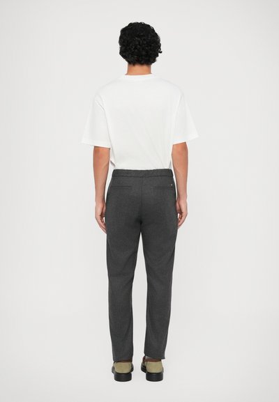 Calças cinzas sob medida com um corte reto, tecido suave, dois bolsos traseiros e uma cintura elástica, combinadas com uma t-shirt branca simples.