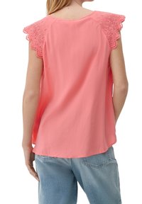 Haut couleur pêche avec manches en dentelle festonnée, texture douce, coupe décontractée et ourlet arrondi. Associé à un jean en denim bleu clair.