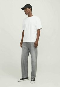 Hvit bomull T-skjorte, avslappet passform, sammen med grå rette jeans. Svart baseball caps og svarte joggesko med hvite detaljer.