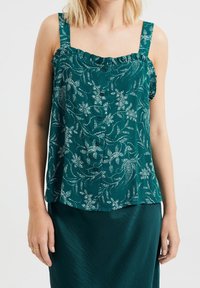 Teal blommig linne med volangaxlar och knappstängning fram, med ett strukturerat tyg och vit botanisk mönstring.