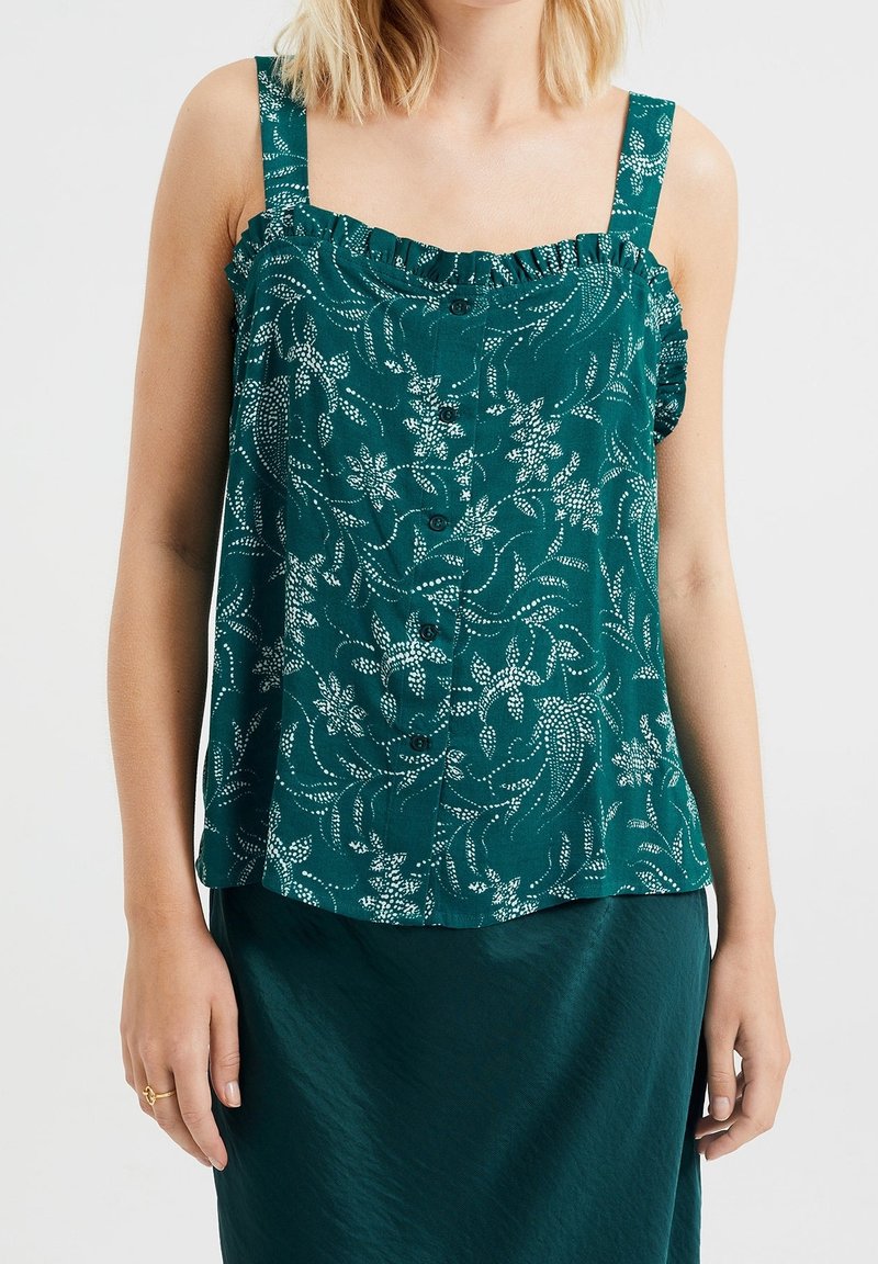 Teal blommig linne med volangaxlar och knappstängning fram, med ett strukturerat tyg och vit botanisk mönstring.