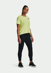 Gai zaļš īsām piedurknēm t-krekls ar brīvu piegriezumu, saskaņots ar melnām sporta biksēm un melnām sporta kurpēm.