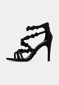 Melna augstpapēžu sandale ar vairākiem plāniem siksniņām, rotāta ar maziem auduma lokiem un potītes sprādzes aizdari.