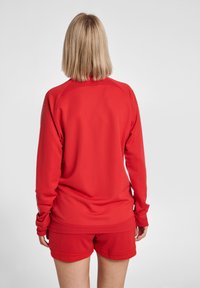 Rotes Sporttop mit langen Ärmeln und strukturiertem Stoff, kombiniert mit passenden roten Shorts. Verfügt über gerippte Akzente und eine lockere Passform.