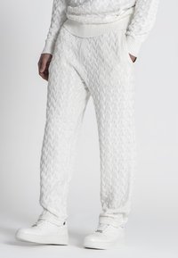 Witte gebreide joggingsbroek met een kabelbreipatroon, voorzien van een geribde tailleband, zijzakken en gecombineerd met witte sneakers.