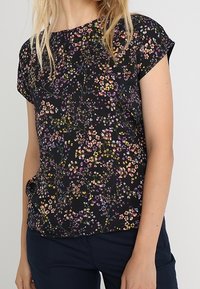 Top de manga corta en tela negra con un estampado floral que presenta flores moradas, amarillas y rosas. Textura suave y ajuste relajado.