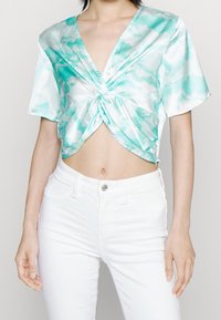 Turkusowa bluzka z węzłem z przodu, wykonana z satynowego materiału, z dekoltem w serek i krótkimi rękawami, w połączeniu z białymi dżinsami o wysokim stanie.