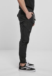 Pantalones cargo negros con cintura ajustable, bolsillos laterales y puños elásticos. Llevados con zapatillas negras con detalles blancos.