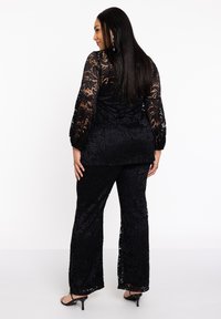 Zwart kant twee-delige set met bloemenpatronen, lange mouwen en brede broekspijpen. Doorzichtige textuur met een stevige onderlaag, afgewerkt met hoge hakken.