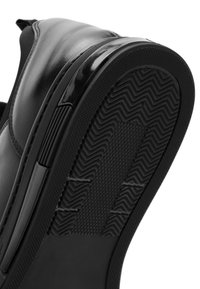 Scarpa nera in pelle con un design elegante, caratterizzata da una tomaia liscia e una suola in gomma nera testurizzata con motivo a zigzag per una migliore aderenza.