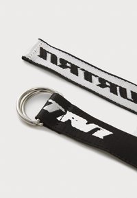 Zwart-wit stoffen band met een zilveren metalen ring. De band heeft contrasterende tekstpatronen en een gestructureerd oppervlak.
