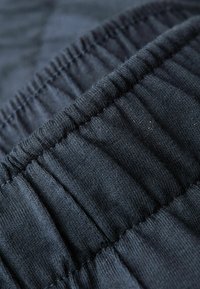 Zwarte stof met een geplooid textuur en elastische tailleband, met zichtbare stikseldetails; zachte en gladde oppervlakte.