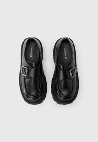 Svarta läderskor med rundad tå, utrustade med ett sidospänne och tjock gummisula med texturerade detaljer. Klassisk och robust design.