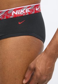 Černé bavlněné kalhotky se vzorovaným elastickým páskem v červené a šedé barvě. Na přední straně je červené logo Nike. Měkká textura, přiléhavý střih.