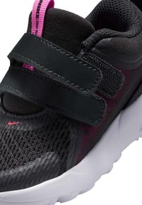 Zapatilla deportiva negra con parte superior de malla y acentos en rosa, correas de Velcro negras y suela blanca acolchada.