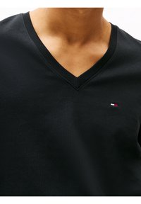 Black cotton V-neck t-shirt featuring a flat knit collar and a small tri-color logo accent on the left chest. Soft texture, fitted design.