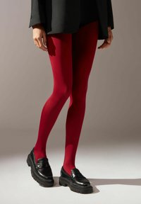 Röda ogenomskinliga strumpbyxor gjorda av stretchy material, med en slät yta. Kombineras med svarta tunga loafers för en modern look.
