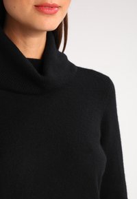 Černý rolákový svetr z jemné vlny. Má volný střih a skládací límec. Textura působ�í hladce s minimálním vzorem.