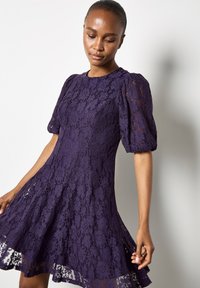 Fioletowa koronkowa sukienka z krótkimi bufkami, dopasowanym gorsetem i rozkloszowaną spódnicą. Posiada kwiatowy wzór koronkowy i przezroczyste akcenty na krawędzi.