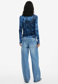 Haut à manches longues, en tissu doux, bleu à motifs, associé à un jean large, bleu clair, avec poches arrière et détails de surpiqûres.