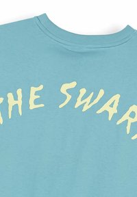 Jasnoniebieska tkanina z off-white stylizowanym napisem "THE SWAR" na górnej części klatki piersiowej w pobliżu okrągłego dekoltu.
