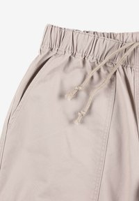 Beżowe spodnie na sznurku z elastycznym paskiem w talii, z bocznymi kieszeniami i gładką, teksturowaną powierzchnią materiału.