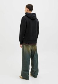 Sudadera negra con capucha de corte holgado, combinada con jeans de pierna ancha que presentan un lavado degradado. El conjunto tiene un aspecto casual y en capas.