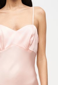 Naine, kes kannab õlgadeta kahvaturoosat satiinist kleiti, millel on õhukesed rihmad ja südamekujuline dekoltee, nähtav õlgadest vööni.