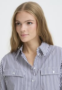 Striped button-up shirt in navy and white cotton. Features a pointed collar and two chest pockets with button closures.